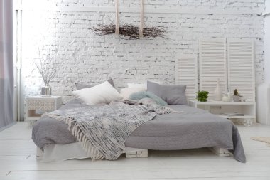 Geniş, şık, modern, beyaz ve açık renkli çatı katı dairesi. Güneş ışığıyla dolu büyük bir oda. tuğla duvar, ahşap zemin, raf, palet yatak ve büyük pencere. Her şey beyaz ve gri renkli..