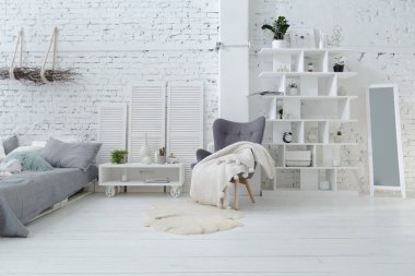 Geniş, şık, modern, beyaz ve açık renkli çatı katı dairesi. Güneş ışığıyla dolu büyük bir oda. tuğla duvar, ahşap zemin, raf, palet yatak ve büyük pencere. Her şey beyaz ve gri renkli..