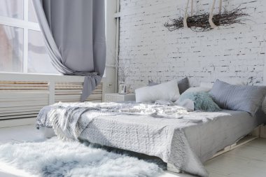 Geniş, şık, modern, beyaz ve açık renkli çatı katı dairesi. Güneş ışığıyla dolu büyük bir oda. tuğla duvar, ahşap zemin, raf, palet yatak ve büyük pencere. Her şey beyaz ve gri renkli..