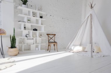 Geniş, şık, modern, beyaz ve açık renkli çatı katı dairesi. Güneş ışığıyla dolu büyük bir oda. Tuğla duvar, ahşap zemin, raf, palet yatak ve çadır şeklinde çocuk evi. Her şey beyaz ve gri renkli..