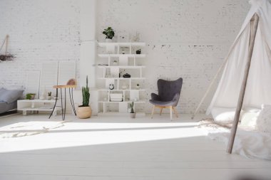 Geniş, şık, modern, beyaz ve açık renkli çatı katı dairesi. Güneş ışığıyla dolu büyük bir oda. Tuğla duvar, ahşap zemin, raf, palet yatak ve çadır şeklinde çocuk evi. Her şey beyaz ve gri renkli..