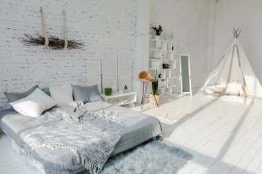 Geniş, şık, modern, beyaz ve açık renkli çatı katı dairesi. Güneş ışığıyla dolu büyük bir oda. tuğla duvar, ahşap zemin, raf, palet yatak ve büyük pencere. Her şey beyaz ve gri renkli..