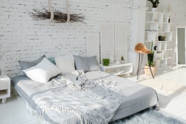 Geniş, şık, modern, beyaz ve açık renkli çatı katı dairesi. Güneş ışığıyla dolu büyük bir oda. tuğla duvar, ahşap zemin, raf, palet yatak ve büyük pencere. Her şey beyaz ve gri renkli..