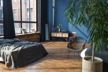 Modern stil, büyük, açık fikirli, sütunları ve yüksek tavanı olan bir stüdyo dairenin karanlık iç mekanı. Koyu mavi astar duvarlar ahşapla süslenmiş. Güneş ışığı dev pencerelerden içeri giriyor..