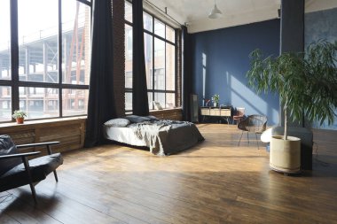 Modern stil, büyük, açık fikirli, sütunları ve yüksek tavanı olan bir stüdyo dairenin karanlık iç mekanı. Koyu mavi astar duvarlar ahşapla süslenmiş. Güneş ışığı dev pencerelerden içeri giriyor..