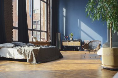 Modern stil, büyük, açık fikirli, sütunları ve yüksek tavanı olan bir stüdyo dairenin karanlık iç mekanı. Koyu mavi astar duvarlar ahşapla süslenmiş. Güneş ışığı dev pencerelerden içeri giriyor..