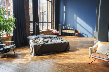 Modern stil, büyük, açık fikirli, sütunları ve yüksek tavanı olan bir stüdyo dairenin karanlık iç mekanı. Koyu mavi astar duvarlar ahşapla süslenmiş. Güneş ışığı dev pencerelerden içeri giriyor..