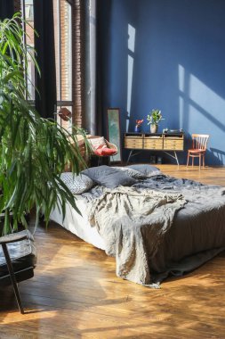 Modern stil, büyük, açık fikirli, sütunları ve yüksek tavanı olan bir stüdyo dairenin karanlık iç mekanı. Koyu mavi astar duvarlar ahşapla süslenmiş. Güneş ışığı dev pencerelerden içeri giriyor..