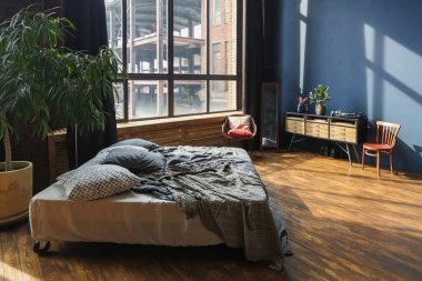 Modern stil, büyük, açık fikirli, sütunları ve yüksek tavanı olan bir stüdyo dairenin karanlık iç mekanı. Koyu mavi astar duvarlar ahşapla süslenmiş. Güneş ışığı dev pencerelerden içeri giriyor..