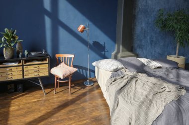 Modern stil, büyük, açık fikirli, sütunları ve yüksek tavanı olan bir stüdyo dairenin karanlık iç mekanı. Koyu mavi astar duvarlar ahşapla süslenmiş. Güneş ışığı dev pencerelerden içeri giriyor..