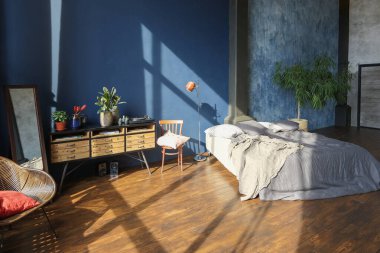 Modern stil, büyük, açık fikirli, sütunları ve yüksek tavanı olan bir stüdyo dairenin karanlık iç mekanı. Koyu mavi astar duvarlar ahşapla süslenmiş. Güneş ışığı dev pencerelerden içeri giriyor..