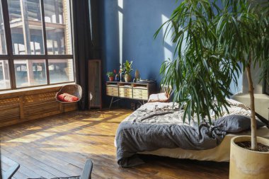 Modern stil, büyük, açık fikirli, sütunları ve yüksek tavanı olan bir stüdyo dairenin karanlık iç mekanı. Koyu mavi astar duvarlar ahşapla süslenmiş. Güneş ışığı dev pencerelerden içeri giriyor..