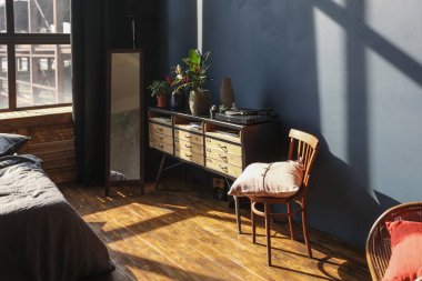 Modern stil, büyük, açık fikirli, sütunları ve yüksek tavanı olan bir stüdyo dairenin karanlık iç mekanı. Koyu mavi astar duvarlar ahşapla süslenmiş. Güneş ışığı dev pencerelerden içeri giriyor..