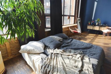 Modern stil, büyük, açık fikirli, sütunları ve yüksek tavanı olan bir stüdyo dairenin karanlık iç mekanı. Koyu mavi astar duvarlar ahşapla süslenmiş. Güneş ışığı dev pencerelerden içeri giriyor..