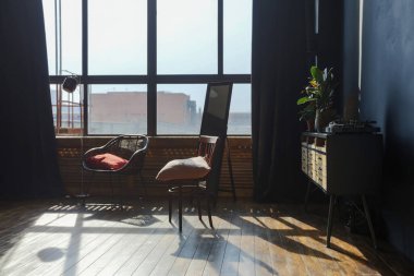 Modern stil, büyük, açık fikirli, sütunları ve yüksek tavanı olan bir stüdyo dairenin karanlık iç mekanı. Koyu mavi astar duvarlar ahşapla süslenmiş. Güneş ışığı dev pencerelerden içeri giriyor..