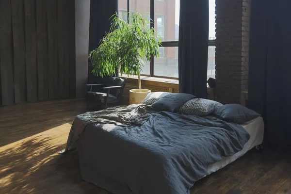 dark interior of a modern stylish huge open-plan loft-style studio apartment with columns and high ceilings. dark blue primed walls are decorated with wood. sunlight enters through huge windows.