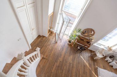 İki katlı, balkon tarzı dekoratif eşyalarla dolu, parlak bir dairede modern bir oda. Beyaz duvarlar, ahşap döşemeler ve eski mobilyalar.