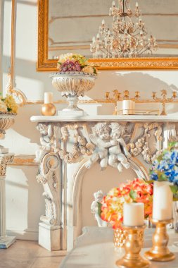 Duvarlarında altın barok süslemeleri ve lüks mobilyaları olan zengin bir daire. Oda batan güneşin ışınlarıyla dolup taşıyor.