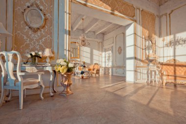Duvarlarında altın barok süslemeleri ve lüks mobilyaları olan zengin bir daire. Oda batan güneşin ışınlarıyla dolup taşıyor.