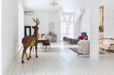 Geniş, parlak bir oturma odası. Modern tasarımı, antika dekorları ve eski tarz şık mobilyaları ve yerden tavana kadar birçok penceresi var.