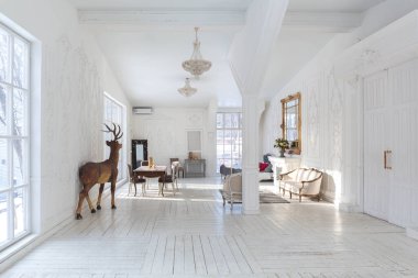 Geniş, parlak bir oturma odası. Modern tasarımı, antika dekorları ve eski tarz şık mobilyaları ve yerden tavana kadar birçok penceresi var.