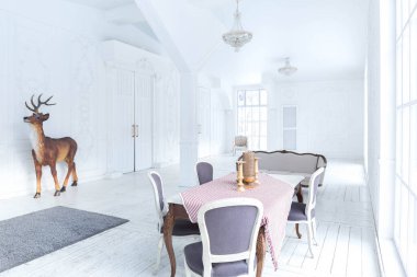 Geniş, parlak bir oturma odası. Modern tasarımı, antika dekorları ve eski tarz şık mobilyaları ve yerden tavana kadar birçok penceresi var.