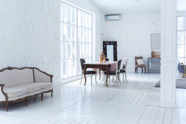 Geniş, parlak bir oturma odası. Modern tasarımı, antika dekorları ve eski tarz şık mobilyaları ve yerden tavana kadar birçok penceresi var.