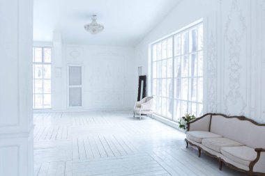 Geniş, parlak bir oturma odası. Modern tasarımı, antika dekorları ve eski tarz şık mobilyaları ve yerden tavana kadar birçok penceresi var.