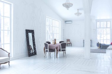 Geniş, parlak bir oturma odası. Modern tasarımı, antika dekorları ve eski tarz şık mobilyaları ve yerden tavana kadar birçok penceresi var.