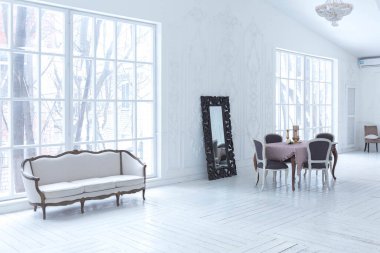 Geniş, parlak bir oturma odası. Modern tasarımı, antika dekorları ve eski tarz şık mobilyaları ve yerden tavana kadar birçok penceresi var.