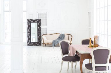 Geniş, parlak bir oturma odası. Modern tasarımı, antika dekorları ve eski tarz şık mobilyaları ve yerden tavana kadar birçok penceresi var.