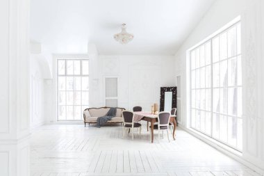 Geniş, parlak bir oturma odası. Modern tasarımı, antika dekorları ve eski tarz şık mobilyaları ve yerden tavana kadar birçok penceresi var.