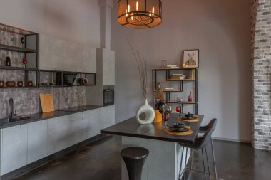 Ortaçağ şatosu tarzında parlak aksanlı, vahşi bir apartman dairesinin modern lüks tasarımı. Yemek pişirmek ya da zaman geçirmek için bir adası olan şık gri bir mutfak.