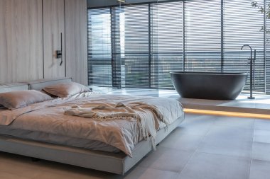 Japon tarzı bej ve siyah renklerde modern minimalist yumuşak tasarım odası. Panjurları olan büyük bir panoramik pencerenin yanında şık bir şekilde ayrılmış bir banyo.