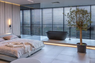 Japon tarzı bej ve siyah renklerde modern minimalist yumuşak tasarım odası. Panjurları olan büyük bir panoramik pencerenin yanında şık bir şekilde ayrılmış bir banyo.