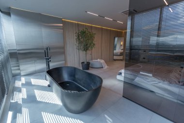 Japon tarzı bej ve siyah renklerde modern minimalist yumuşak tasarım odası. Panjurları olan büyük bir panoramik pencerenin yanında şık bir şekilde ayrılmış bir banyo.