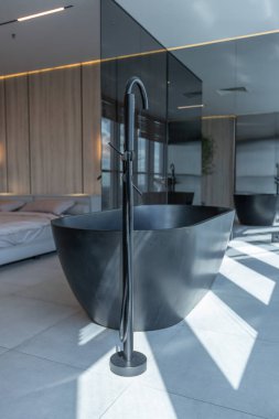 Japon tarzı bej ve siyah renklerde modern minimalist yumuşak tasarım odası. Panjurları olan büyük bir panoramik pencerenin yanında şık bir şekilde ayrılmış bir banyo.