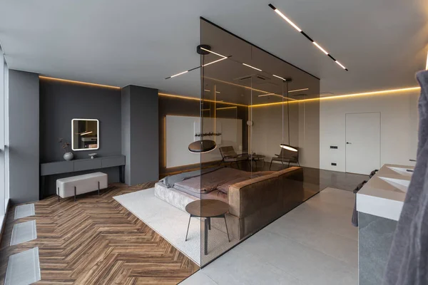 cool expensive interior design of room in prestigious luxury hotel with dark tones with modern LED lighting and stylish furniture. the area with a sink is separated by dark glass from the bedroom