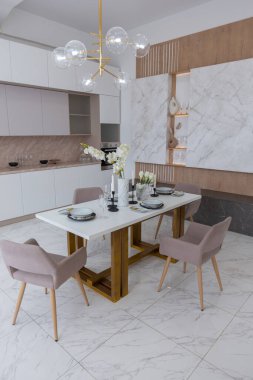 Şık bir mutfak ve açık renkli bir yemek masası. Minimalist tarzda, mermer süslemeli ve kocaman pencereli modern bir apartman dairesi tasarımı. İçeride gün ışığı.