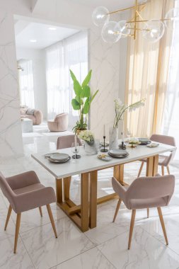 Şık bir mutfak ve açık renkli bir yemek masası. Minimalist tarzda, mermer süslemeli ve kocaman pencereli modern bir apartman dairesi tasarımı. İçeride gün ışığı.