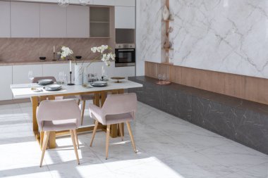 Şık bir mutfak ve açık renkli bir yemek masası. Minimalist tarzda, mermer süslemeli ve kocaman pencereli modern bir apartman dairesi tasarımı. İçeride gün ışığı.