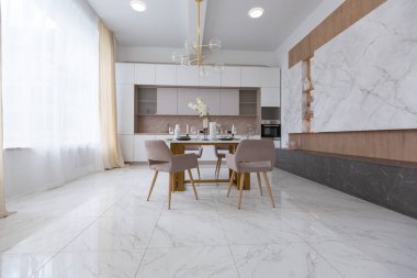 Şık bir mutfak ve açık renkli bir yemek masası. Minimalist tarzda, mermer süslemeli ve kocaman pencereli modern bir apartman dairesi tasarımı. İçeride gün ışığı.