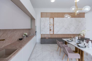 Şık bir mutfak ve açık renkli bir yemek masası. Minimalist tarzda, mermer süslemeli ve kocaman pencereli modern bir apartman dairesi tasarımı. İçeride gün ışığı.
