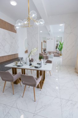 Şık bir mutfak ve açık renkli bir yemek masası. Minimalist tarzda, mermer süslemeli ve kocaman pencereli modern bir apartman dairesi tasarımı. İçeride gün ışığı.