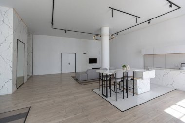 Güneşli bir günde mermer süslemeli pahalı bir evin minimalist modern lüks tasarımı. Alçılı beyaz duvarlar, parke, dekoratif ışıklandırma ve içeride kimse yok.