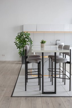 Güneşli bir günde pahalı bir evin minimalist modern lüks tasarımında yüksek bar tabureleri olan mutfak ve yemek adası. Alçılı beyaz duvarlar, parke, dekoratif ışıklandırma ve içeride kimse yok.