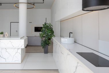 Güneşli bir günde pahalı bir evin minimalist modern lüks tasarımında yüksek bar tabureleri olan mutfak ve yemek adası. Alçılı beyaz duvarlar, parke, dekoratif ışıklandırma ve içeride kimse yok.