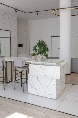 Güneşli bir günde pahalı bir evin minimalist modern lüks tasarımında yüksek bar tabureleri olan mutfak ve yemek adası. Alçılı beyaz duvarlar, parke, dekoratif ışıklandırma ve içeride kimse yok.