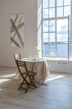 İki kişilik romantik masa, geniş bir pencerenin önünde modern tarzda aydınlık duvarları ve ahşap zemini olan bir dairede servis edilir..