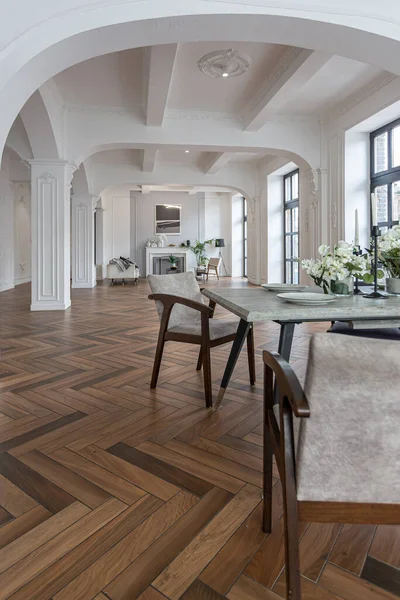 stock image a view of a set dining table in a chic expensive bright interior of a huge living room in a historic mansion with arched arches, columns and white walls decorated with ornaments and stucco.